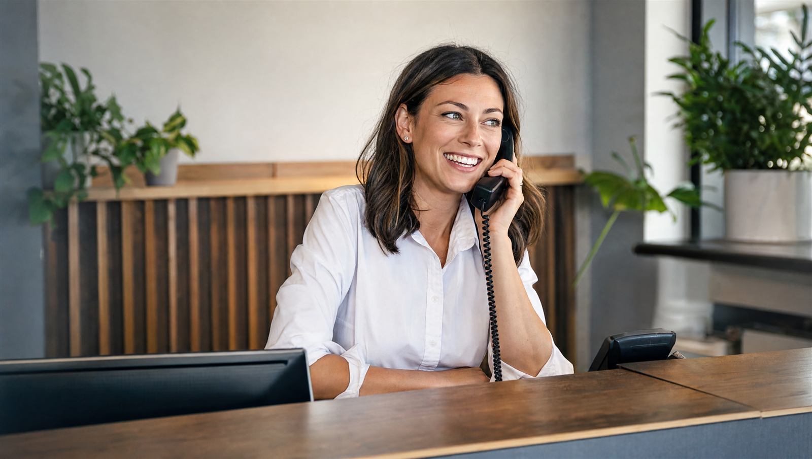 Business owner answering a phone call within seconds of a lead coming in, laptop and phone side by side on a job-site desk